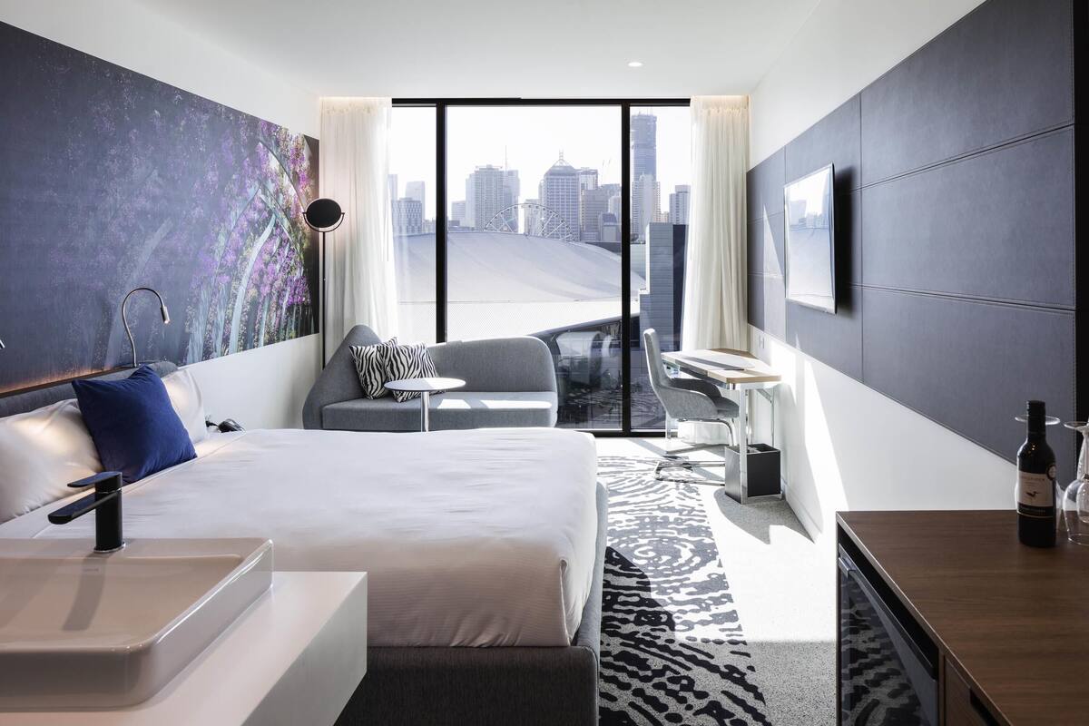 Una habitación de hotel moderna con una cama grande, un escritorio, una silla, una mesita y vistas a la silueta urbana.