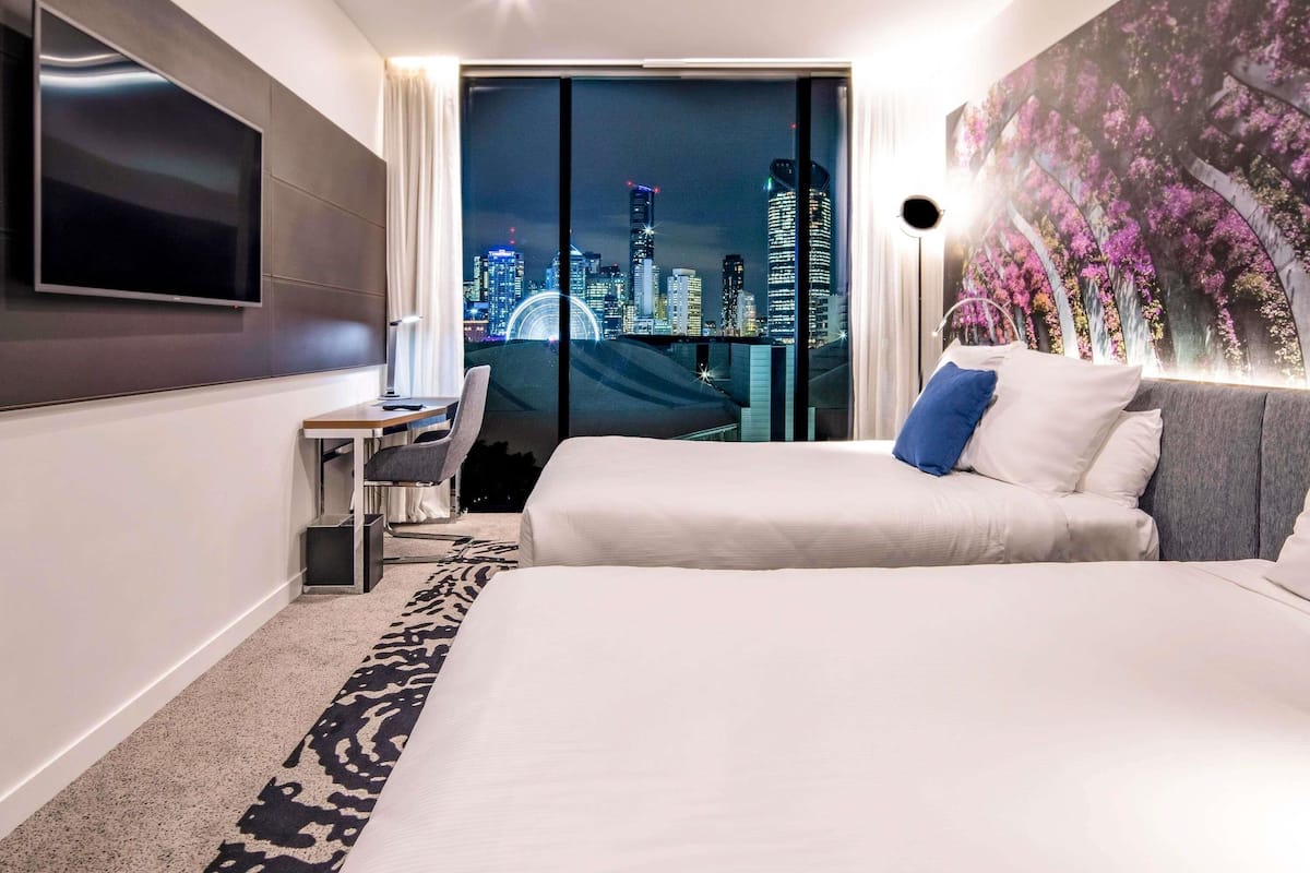 Habitación de hotel con cama, escritorio, silla, televisor y vista a la ciudad.