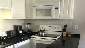 Une cuisine avec des meubles blancs, un four à micro-ondes, une cuisinière, une bouilloire, une machine à café et un lave-vaisselle.