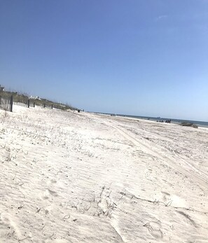 Une plage de sable avec une clôture en bois et un ciel dégagé.
