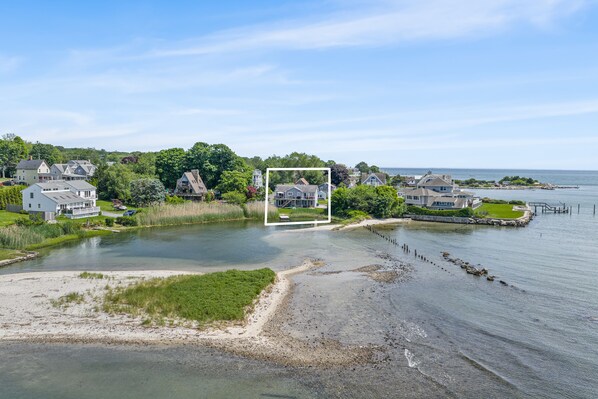En ejendom ved kysten med et stort hus omgivet af vand, en anløbsbro og en mole.