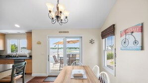 A dining area with a wooden table, chairs, and a chandelier. There are windows with views of the outdoors.