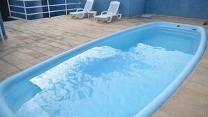 A swimming pool with a tiled deck and two white lounge chairs. - Hotel Gramado de Campos (Campos)