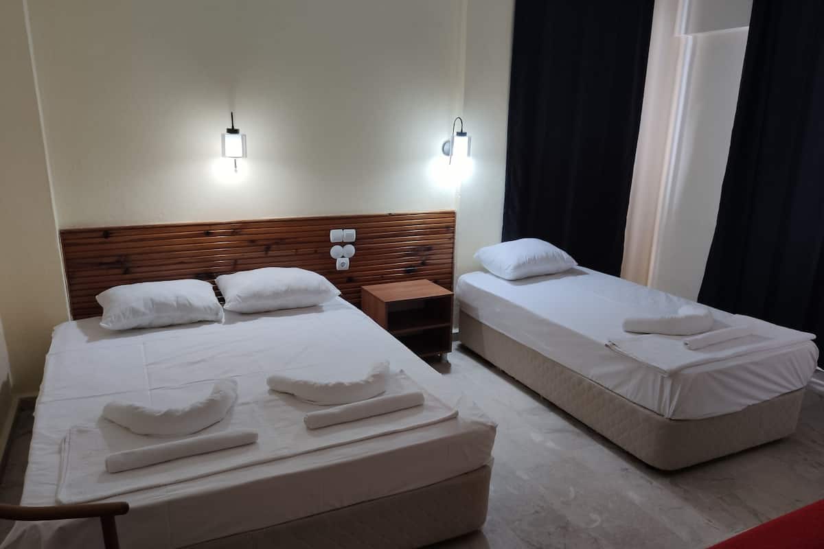 A hotel room with two beds, each with white linens and towels. There are wall-mounted light fixtures above the beds and a wooden headboard.