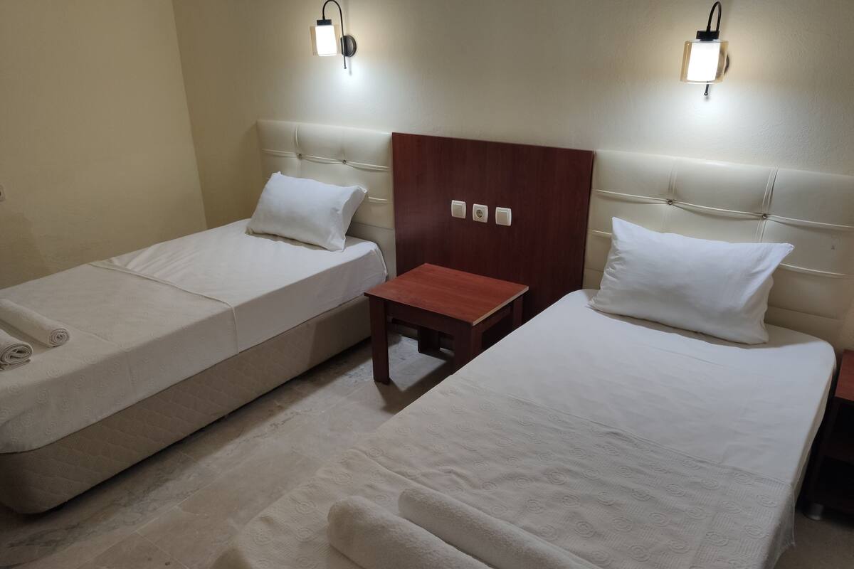A hotel room with two single beds, a small wooden table, and two wall-mounted light fixtures.