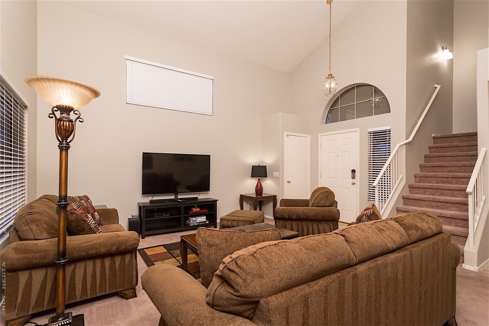 A living room with a flat-screen TV, two sofas, a coffee table, a lamp, and a staircase.
