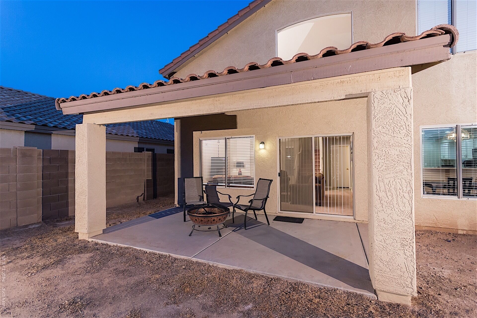 A covered patio with a fire pit, outdoor seating, and sliding glass doors leading to a room.