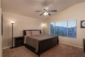 A bedroom with a bed, bedside lamps, a ceiling fan, a window with blinds, and a wall clock. - Arrowhead Area, Quiet, Comfy, 4 TVs (Peoria)