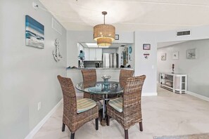 A dining area with wicker chairs, a glass table, and a hanging light fixture.