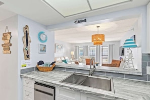 A modern kitchen with a built-in dishwasher, a stainless steel sink, and a large window overlooking a living area.