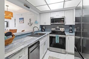 A modern kitchen with white cabinets, stainless steel appliances, a marble countertop, and a hanging light fixture.