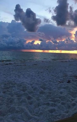 A beach with waves and a sunset in the background.