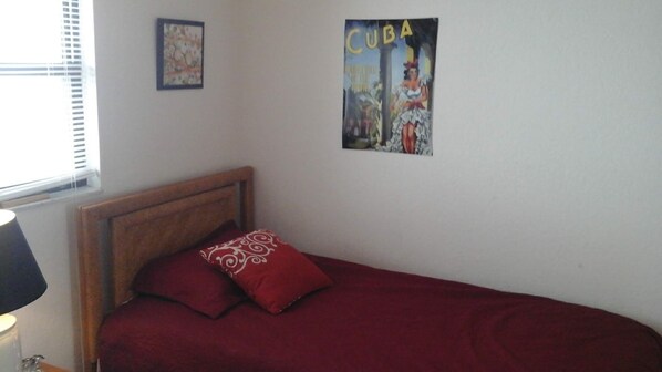 A small bedroom with a single bed, a wooden headboard, and a red bedspread.