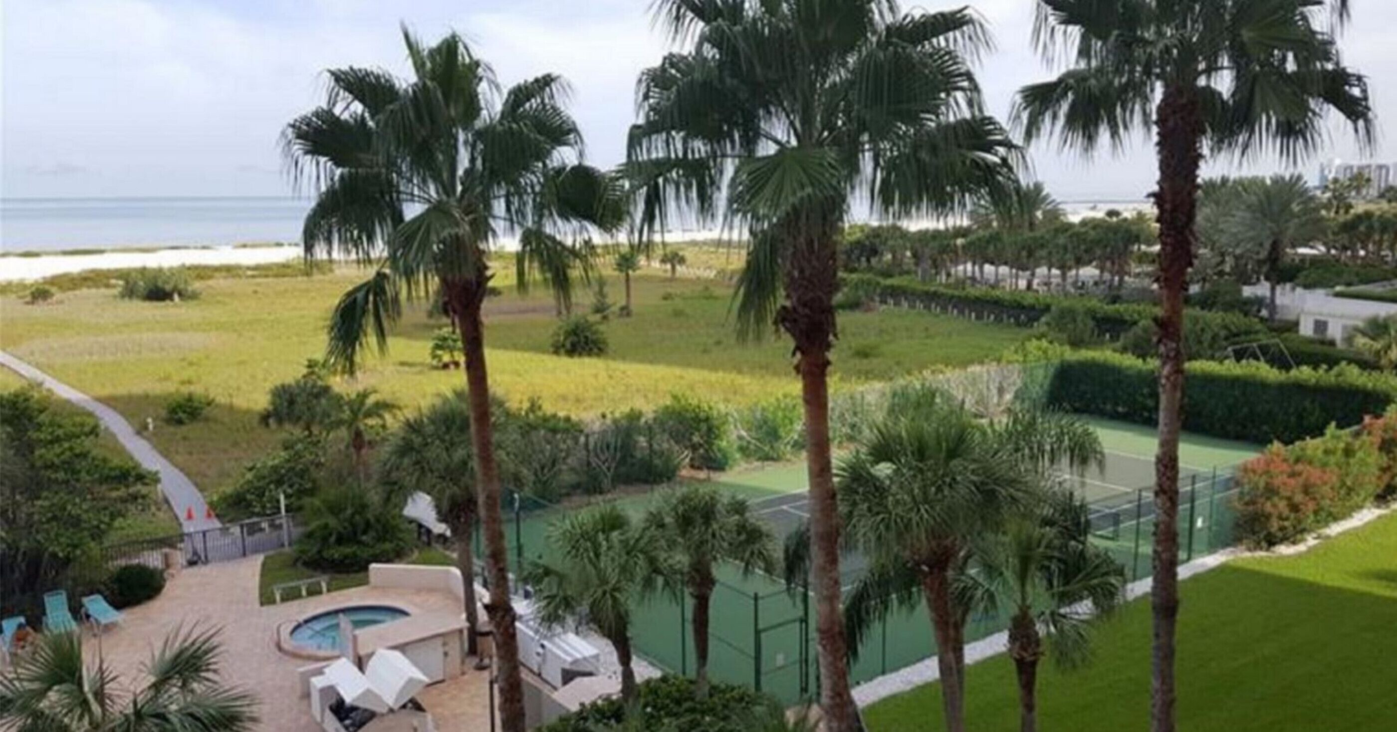 A resort with a pool area, palm trees, and a tennis court.