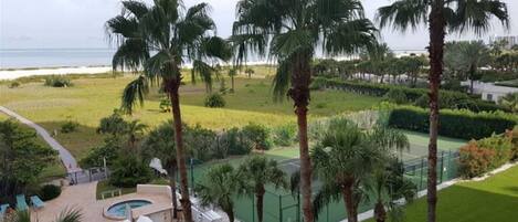 A resort with a pool area, palm trees, and a tennis court.