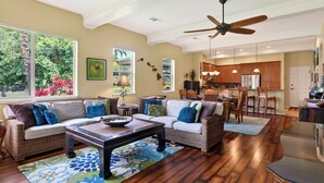 A spacious living area with a large window, a ceiling fan, and a kitchen in the background. - Mauna Lani: Enjoy golf; snorkeling, helicopter tours Flexible cancellation terms (Kamuela)