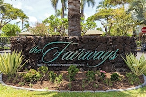 Um letreiro com 'the Fairways' escrito em uma parede de pedra, cercado por plantas tropicais e palmeiras.