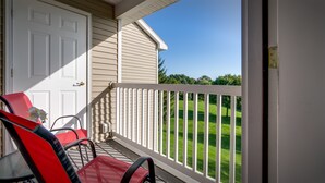 A balcony with a white railing, two red chairs, and a white door.