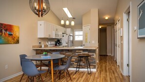 A modern kitchen with white cabinets, a dining area with a round table and chairs, and a hallway with wooden flooring.