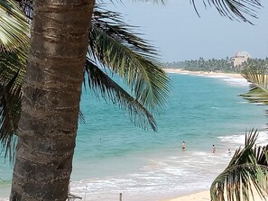 A beach with clear turquoise water, palm trees, and a distant building.