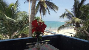 A table with a floral tablecloth, a vase with a red flower, and two white cups on a balcony overlooking a beach with palm trees and the ocean. - Githmini Beach Guest House & Toures (Hikkaduwa)