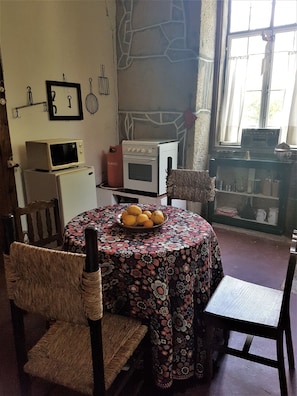 Un coin repas avec une table ronde recouverte d’une nappe à motifs floraux, entourée de chaises en osier. Un bol de citrons est posé sur la table.