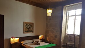 A bedroom with a bed, two bedside tables, a chandelier, a painting, and a window with a view. - Casa da Vila (Penamacor)