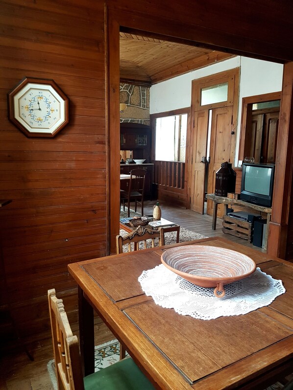 A wooden dining table with a lace doily, a wooden chair, and a clock on the wall.