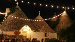 A rustic building with stone roofs and string lights, featuring a dining area with chairs and a table. - Tenuta Antico Leccio (Gioia del Colle)