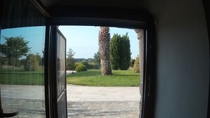 A view through an open door to a stone patio with a lawn and trees. - Tenuta Antico Leccio (Gioia del Colle)