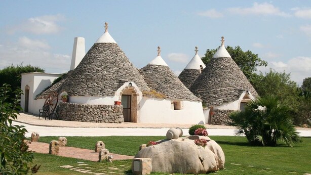 A traditional stone-roofed building with a central entrance and a small garden area with a large rock and potted plants. - Tenuta Antico Leccio (Gioia del Colle)
