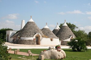 A traditional stone-roofed building with a central entrance and a small garden area with a large rock and potted plants. - Tenuta Antico Leccio (Gioia del Colle)