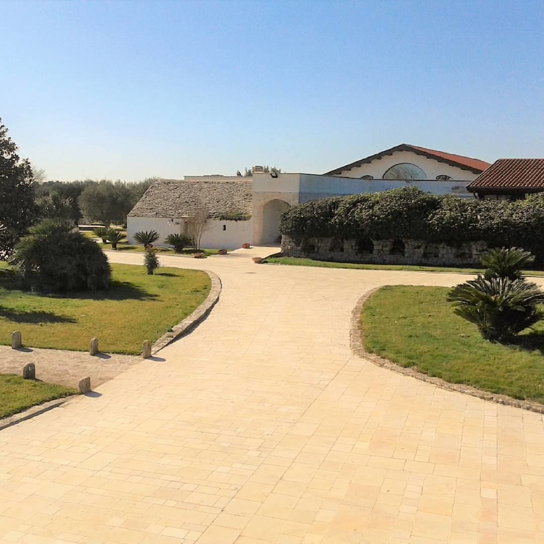 A paved pathway leading to a building with a tiled roof and a stone wall.