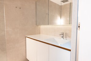 A modern bathroom with a white sink, a large mirror, and beige tiled walls.