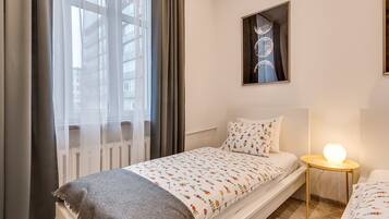 A modern bedroom with a bed, a bedside table with a lamp, a window with curtains, and a wall-mounted artwork.