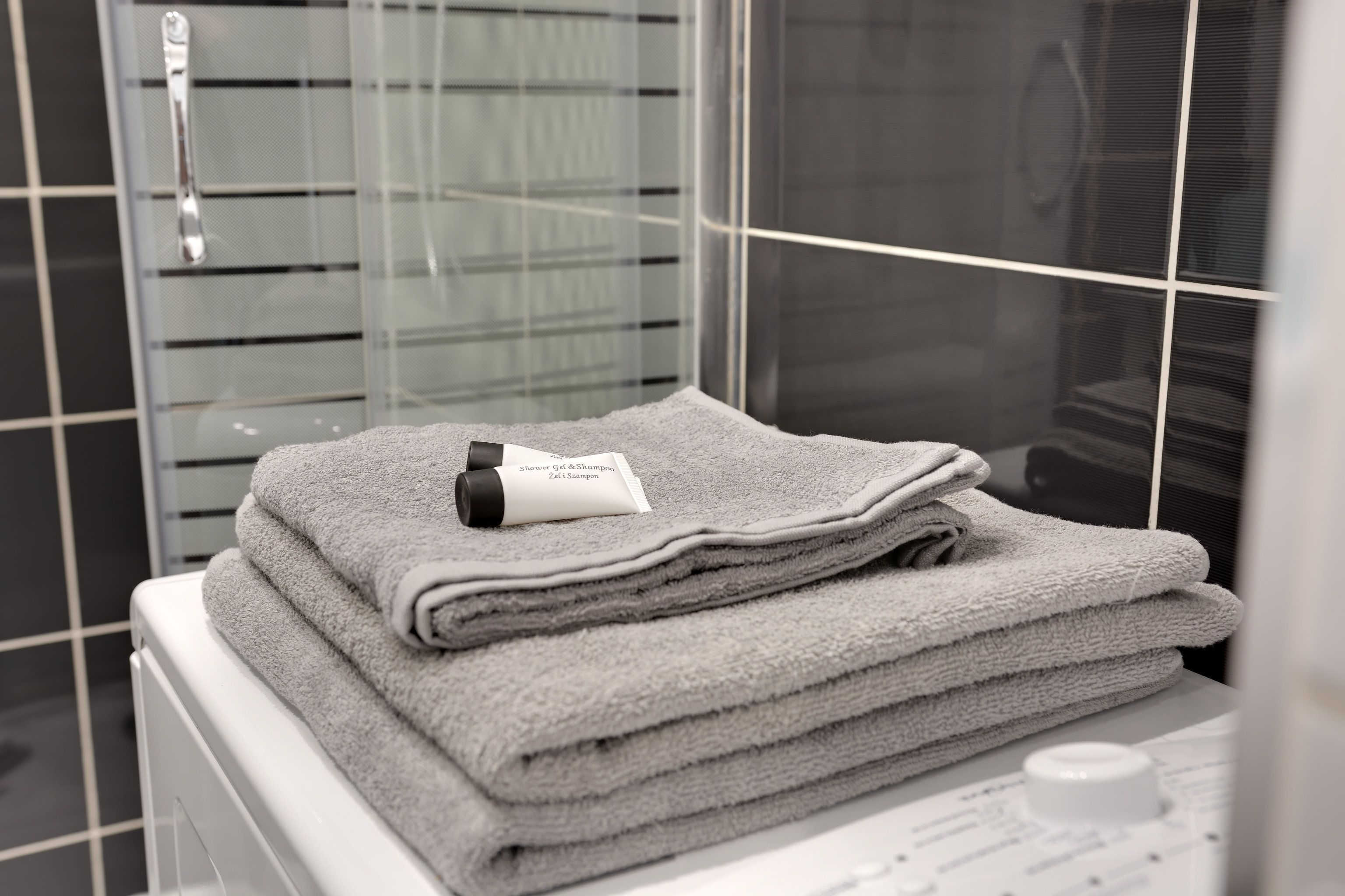 A stack of folded towels on a white surface in a bathroom with a glass shower door and a white radiator.