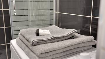 A stack of folded towels on a white surface in a bathroom with a glass shower door and a white radiator.