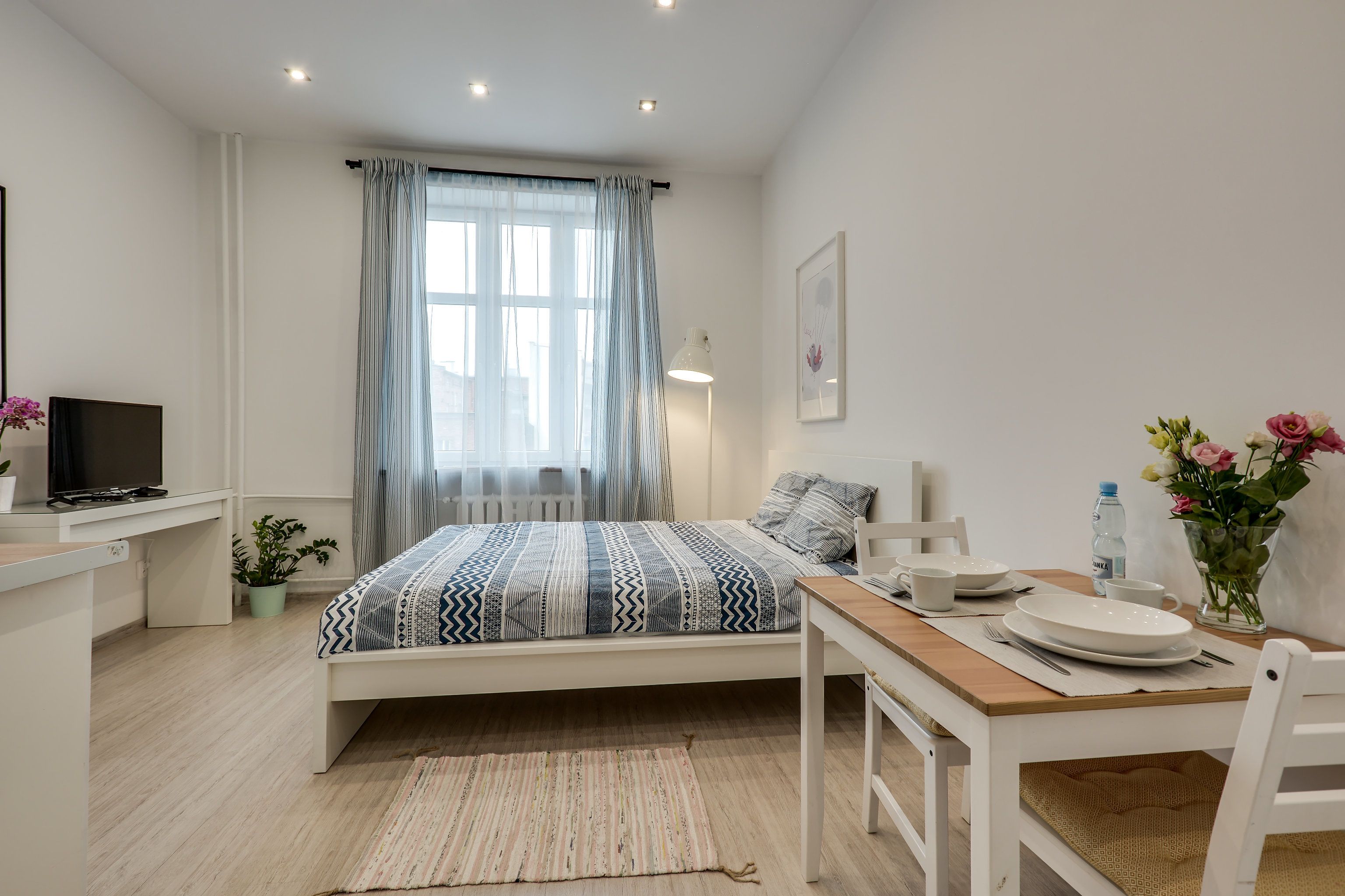 Een moderne slaapkamer met een bed, nachtkastje, lamp en een zithoek met een tafel en stoelen.