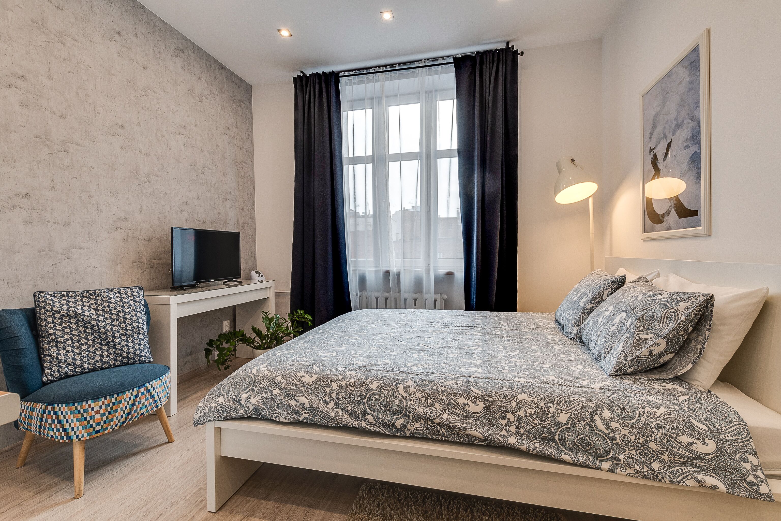 A modern bedroom with a bed, a desk with a TV, a chair, and a window with curtains.