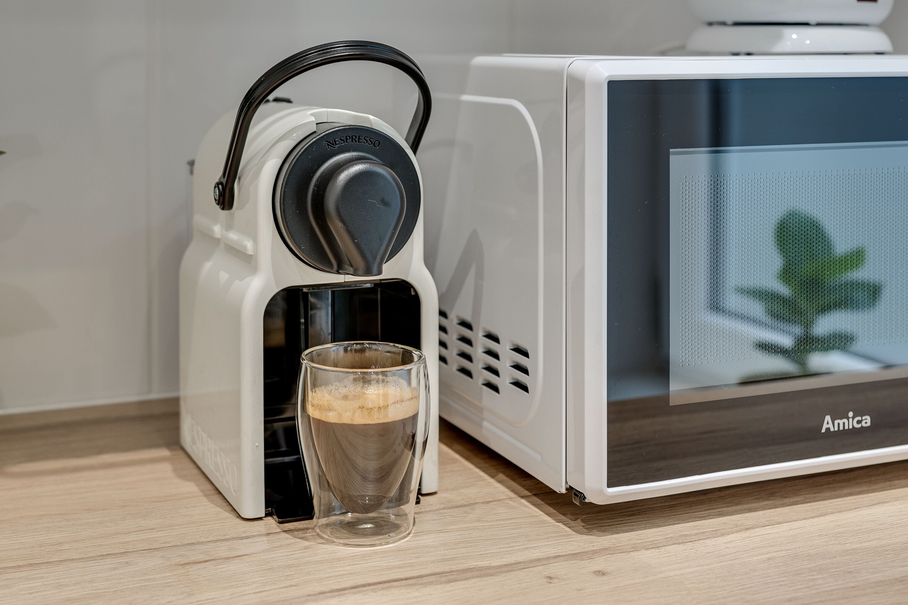 A coffee machine with a glass cup filled with coffee beside it.