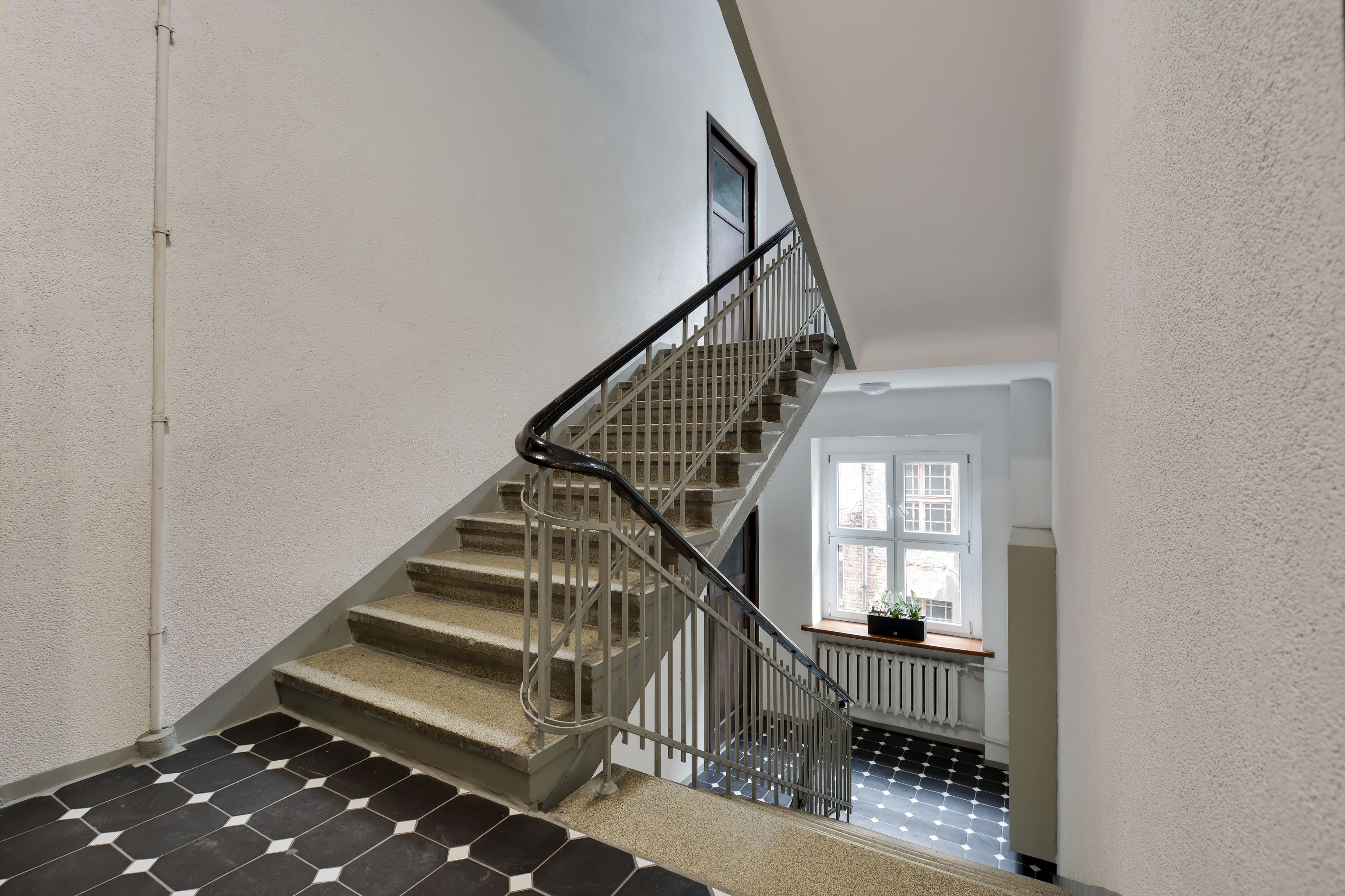 A staircase with a metal railing, a tiled floor, and a window with a plant on the landing.