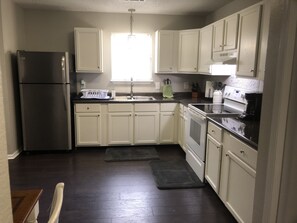A kitchen with white cabinets, a stainless steel refrigerator, a sink, and a stove.