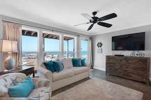 Enjoy the ocean view from this living room with a large window, sofa, armchair, and television.