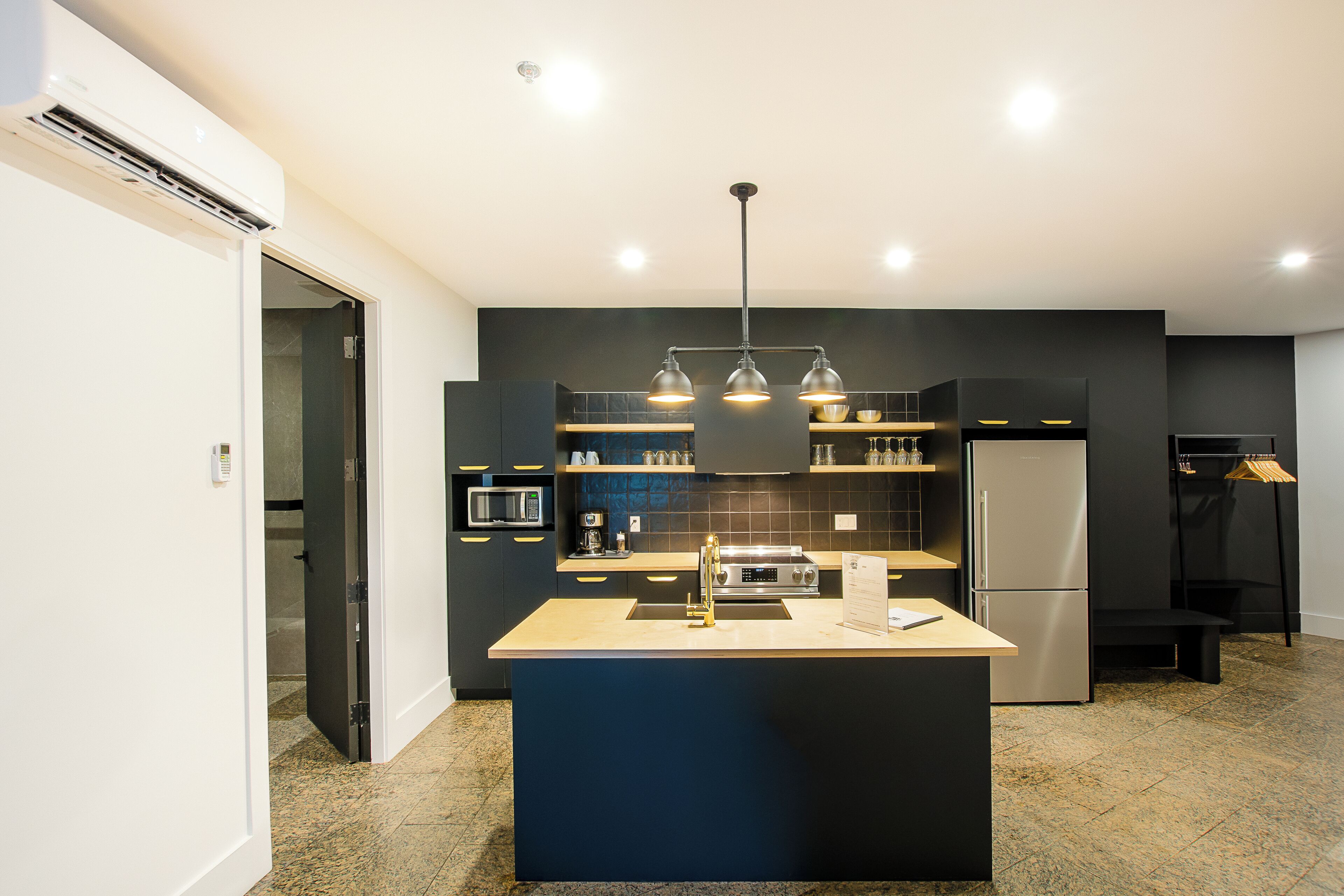 Une cuisine moderne dotée d’un îlot central, d’appareils électroménagers intégrés et de luminaires suspendus.