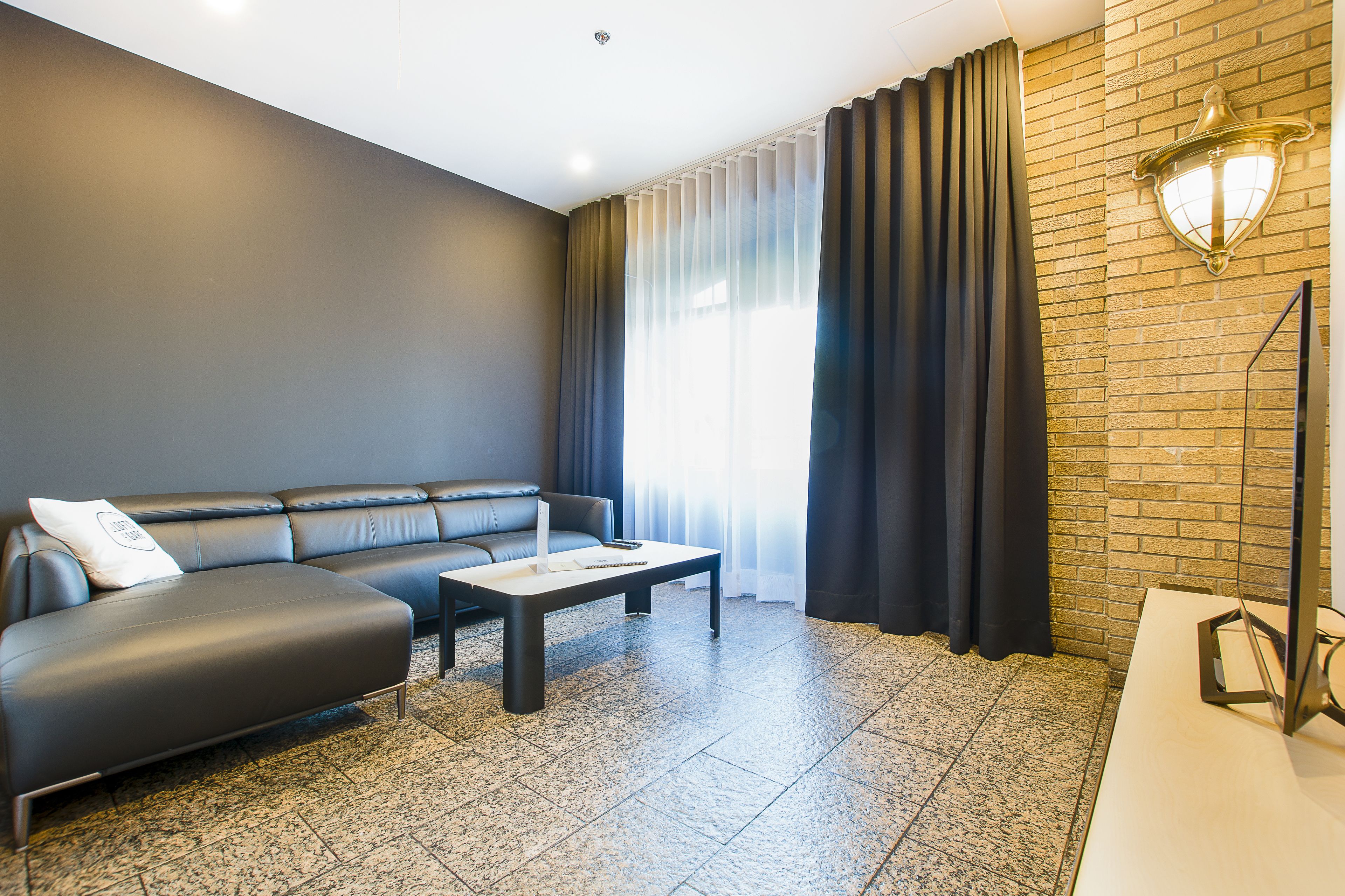 Un salon moderne avec un canapé d’angle, une table basse et un mur décoratif en briques.