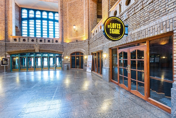 A spacious lobby with a high ceiling and large windows, a prominent sign for 'The Loft at the Gare', and a brick facade.