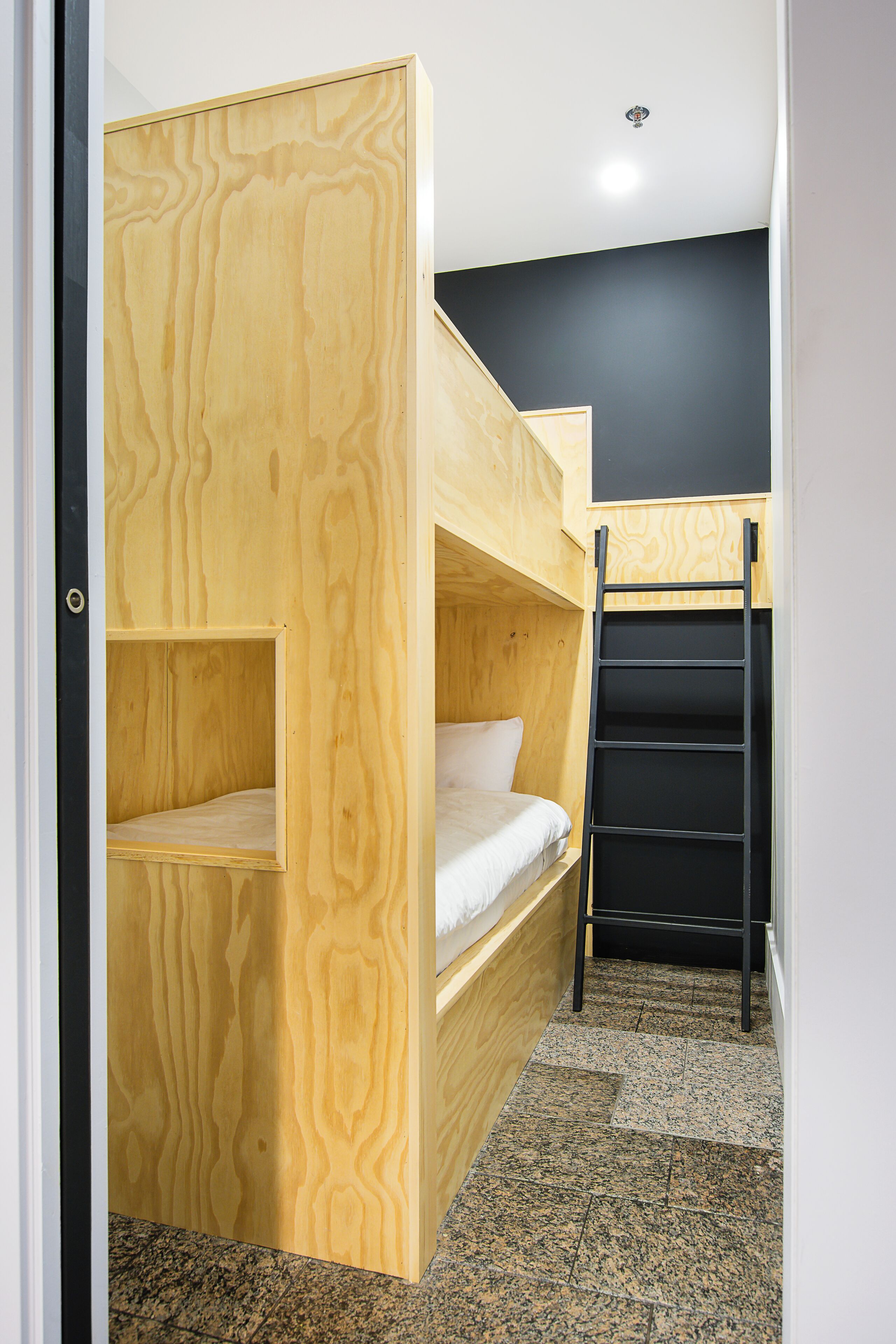 A bunk bed room with a wooden bunk bed and a black ladder.