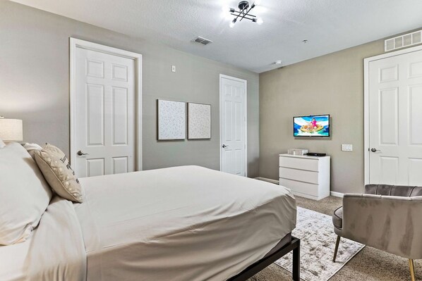 A bedroom with a bed, a dresser, a television, and two doors.