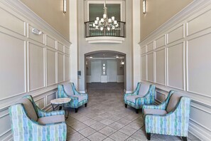 A lobby with a high ceiling, a chandelier, and a view of a door at the end.