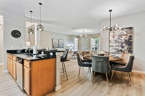 A modern kitchen with a central island, dining area with chairs, and a chandelier. - Fantastic balcony view 3BR near Epic Universe! (Orlando)